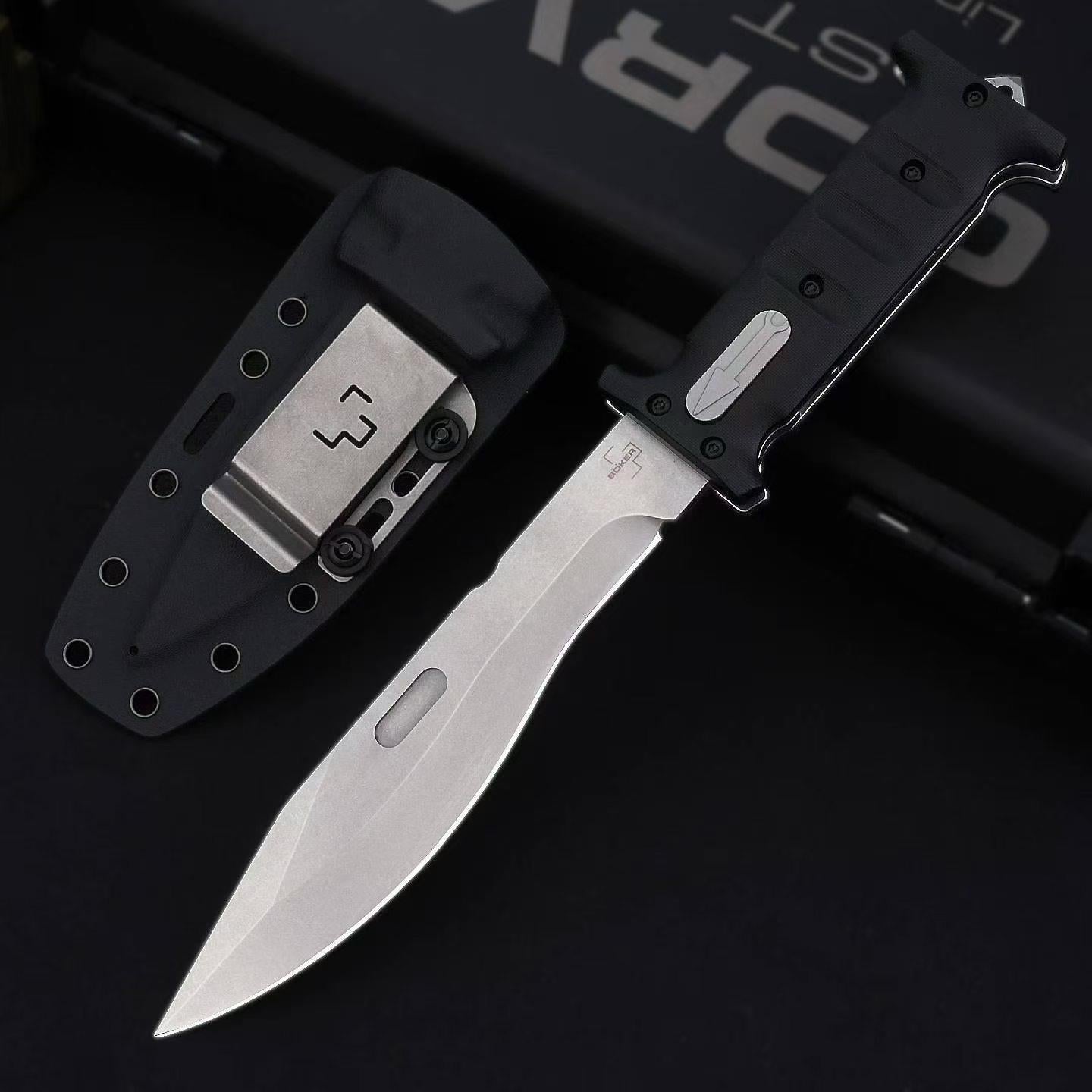 An open folding knife with a silver blade featuring a fuller and a black textured handle, displayed next to a black hard sheath with a metal clip and eyelets, set against a dark background.