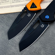 A close-up of two open tactical folding knives with black blades. The knife on the left has an orange handle, and the knife on the right has a black handle with a blue pivot screw, displayed on a textured grey surface.