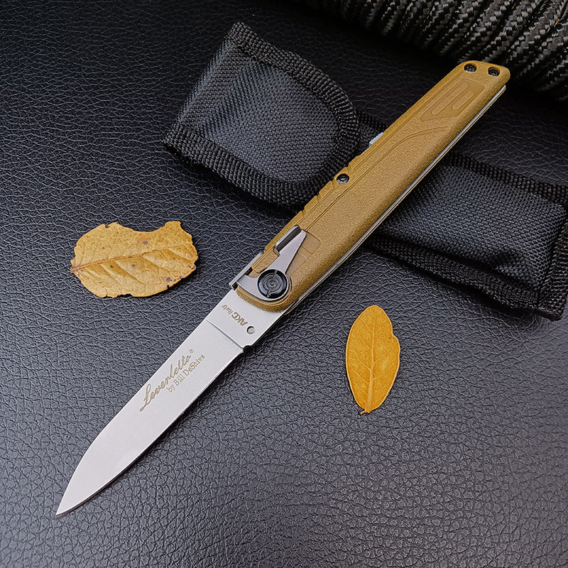 An open tan-handled folding knife displayed with its black nylon carrying pouch and dried yellow leaves on a leather surface.