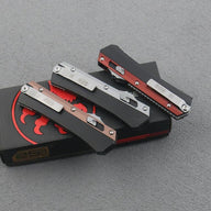 Three closed out-the-front knives showing their silver pocket clips and engraved text, resting on a black and red box on a dark surface.
