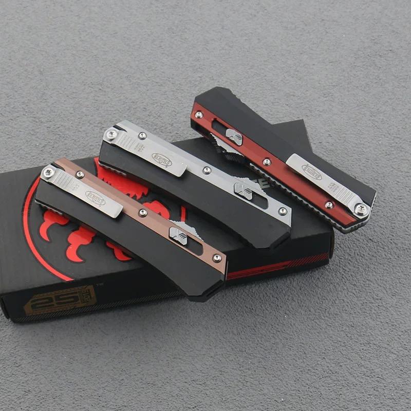 Three closed out-the-front knives showing their silver pocket clips and engraved text, resting on a black and red box on a dark surface.