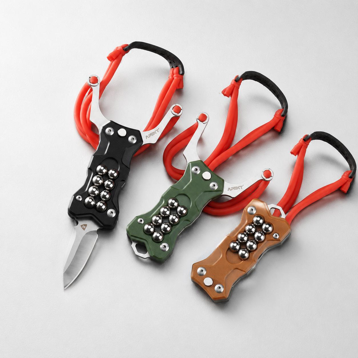 Three EDC multi-tool slingshots in black, green, and tan G10 handles, featuring stainless steel forks and red rubber bands, displayed on a white background. The black model has its blade deployed.
