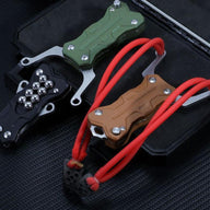 Three EDC slingshots with black, green, and tan G10 handles, displayed on a dark surface next to a black storage case.