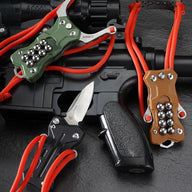 Three EDC slingshots in black, green, and tan G10 handles, displayed together on a black tactical rifle, with the black model featuring the knife blade deployed.