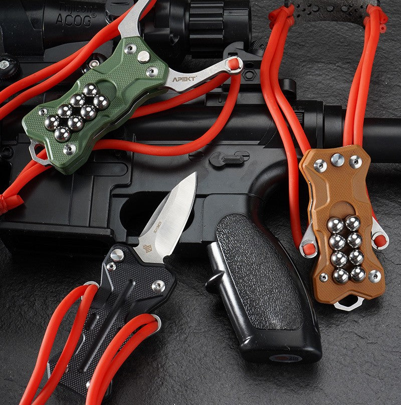 Three EDC slingshots in black, green, and tan G10 handles, displayed together on a black tactical rifle, with the black model featuring the knife blade deployed.