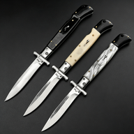 Three open Italian stiletto folding knives with silver blades and crossguards, featuring black, creamy white, and black-and-white marbled handles, arranged diagonally on a dark background.