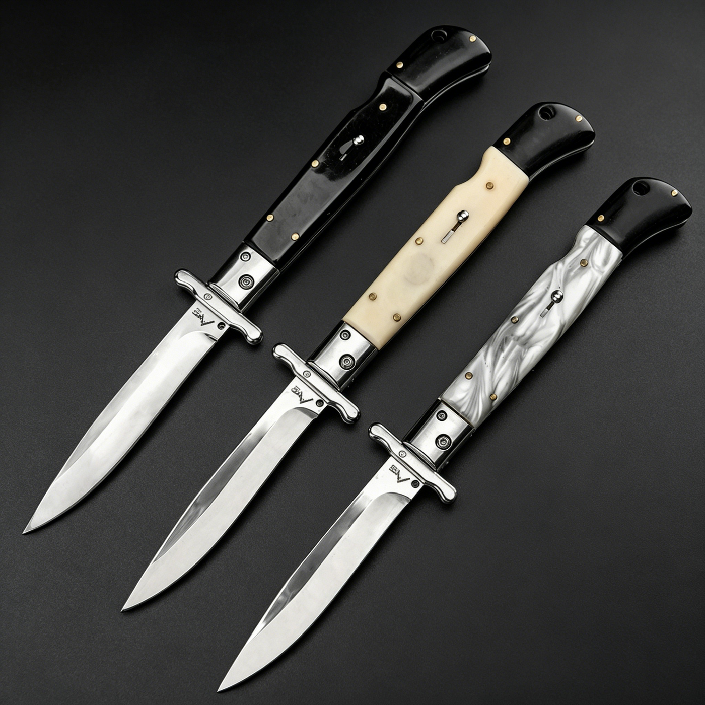 Three open Italian stiletto folding knives with silver blades and crossguards, featuring black, creamy white, and black-and-white marbled handles, arranged diagonally on a dark background.