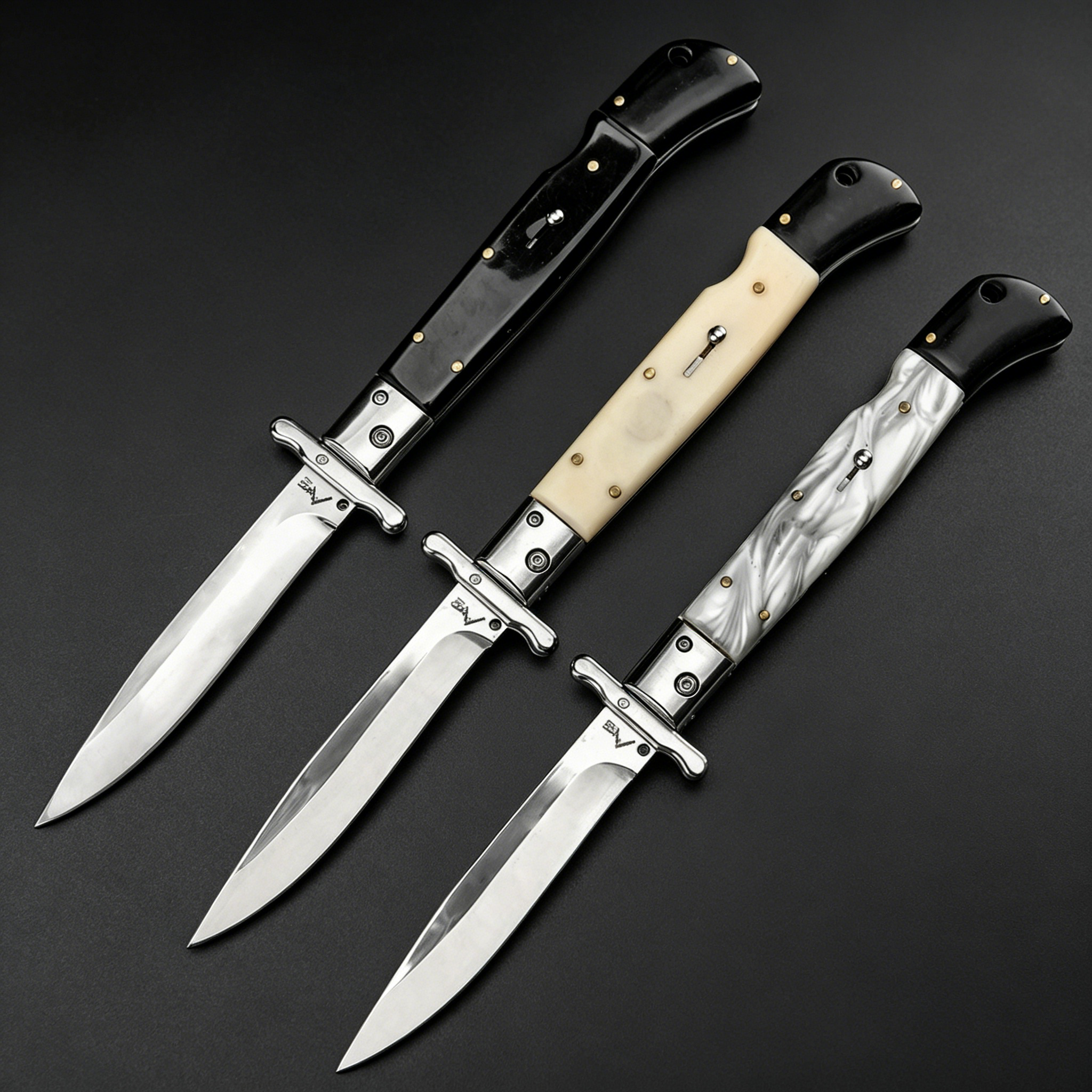 Three open Italian stiletto folding knives with silver blades and crossguards, featuring black, creamy white, and black-and-white marbled handles, arranged diagonally on a dark background.