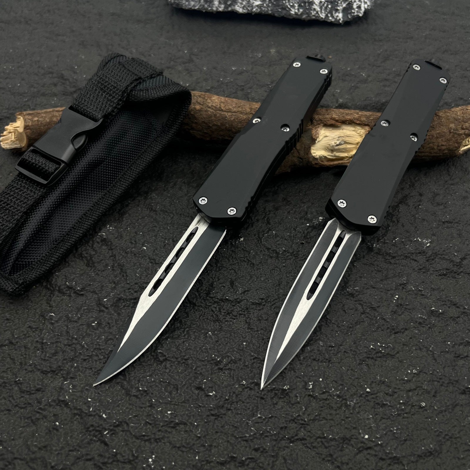 Two black OTF knives with silver blades and different blade shapes, displayed with a black nylon sheath on a rough textured surface with wood.