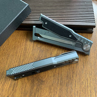 Two closed tactical folding knives with grey handles and black inserts, resting on a wooden surface.