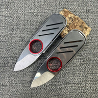 Two open EDC folding knives with silver bodies and red rings, displayed next to a small wood block on a grey textured surface.