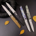 Two open and two closed folding knives arranged diagonally on a dark leather surface next to a thick rope and dried autumn leaves.
