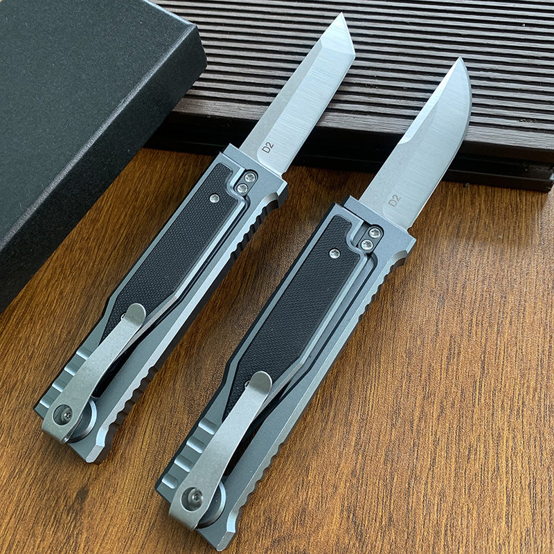 Two tactical folding knives displayed from the back, showing the pocket clips and D2 marking on the blades.