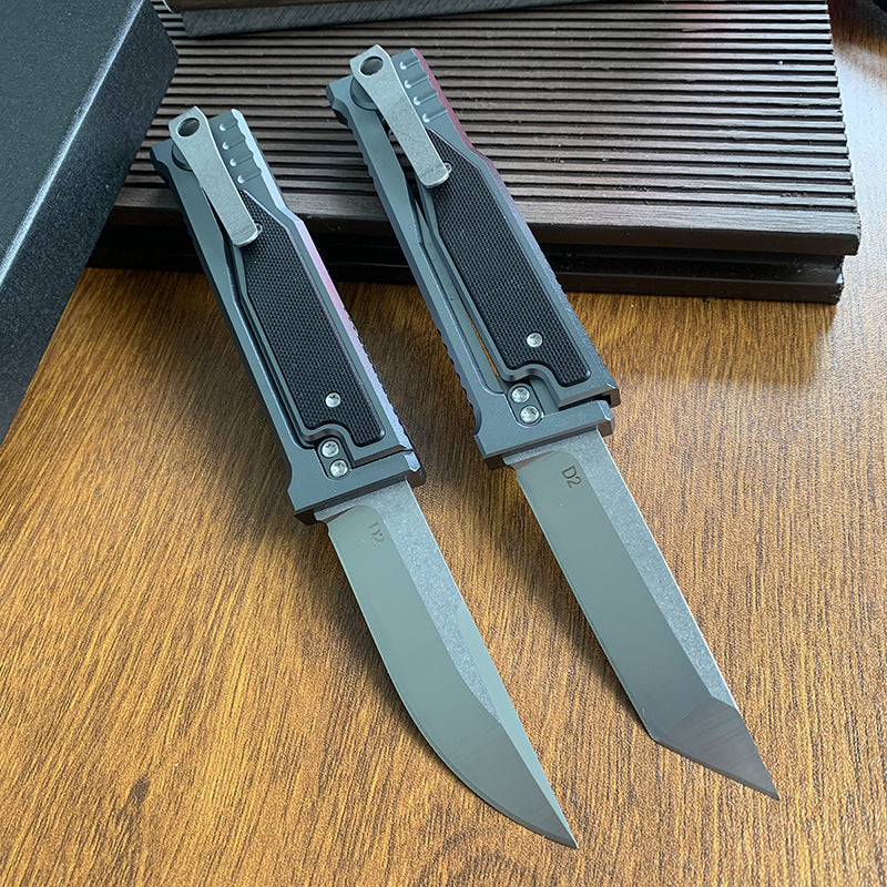 A back side view of two tactical folding knives resting on a wooden surface.