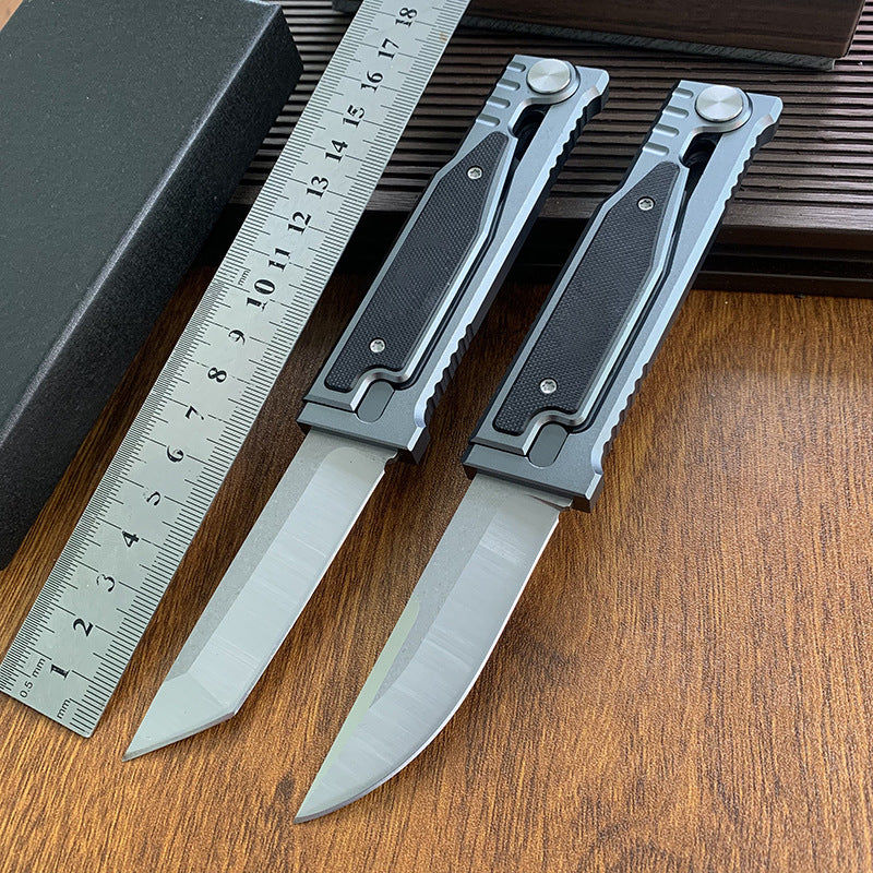 Two tactical folding knives with different blade shapes (tanto and drop point) displayed next to a ruler on a wooden surface.
