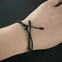 A close-up of a wrist wearing a black tactical handcuff key bracelet, highlighting the adjustable sliding ring and knot details, on a dark background.