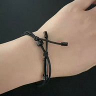 A close-up of a wrist wearing a black tactical handcuff key bracelet, highlighting the adjustable sliding ring and knot details, on a dark background.