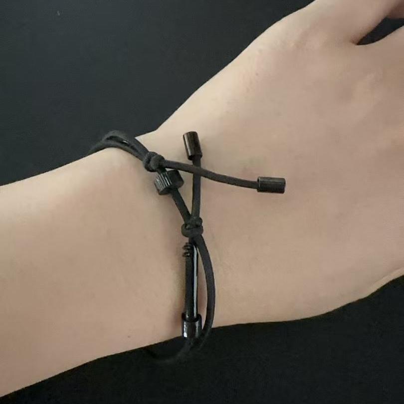 A close-up of a wrist wearing a black tactical handcuff key bracelet, highlighting the adjustable sliding ring and knot details, on a dark background.