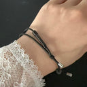A close-up of a wrist wearing a black tactical handcuff key bracelet, showing the metal key tip, adjustable cord, and white lace sleeve, on a dark background.