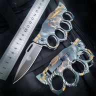 An open and a closed custom graphic knuckle duster knife displayed with a ruler on a tactical bag, showing the overall length and size for reference.