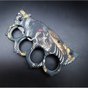 A closed folding knuckle duster knife showcasing the detailed wolf, skull, and gold rose graphic design on the handle, on a dark background.