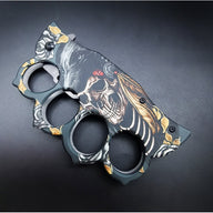 A closed folding knuckle duster knife showcasing the detailed wolf, skull, and gold rose graphic design on the handle, on a dark background.