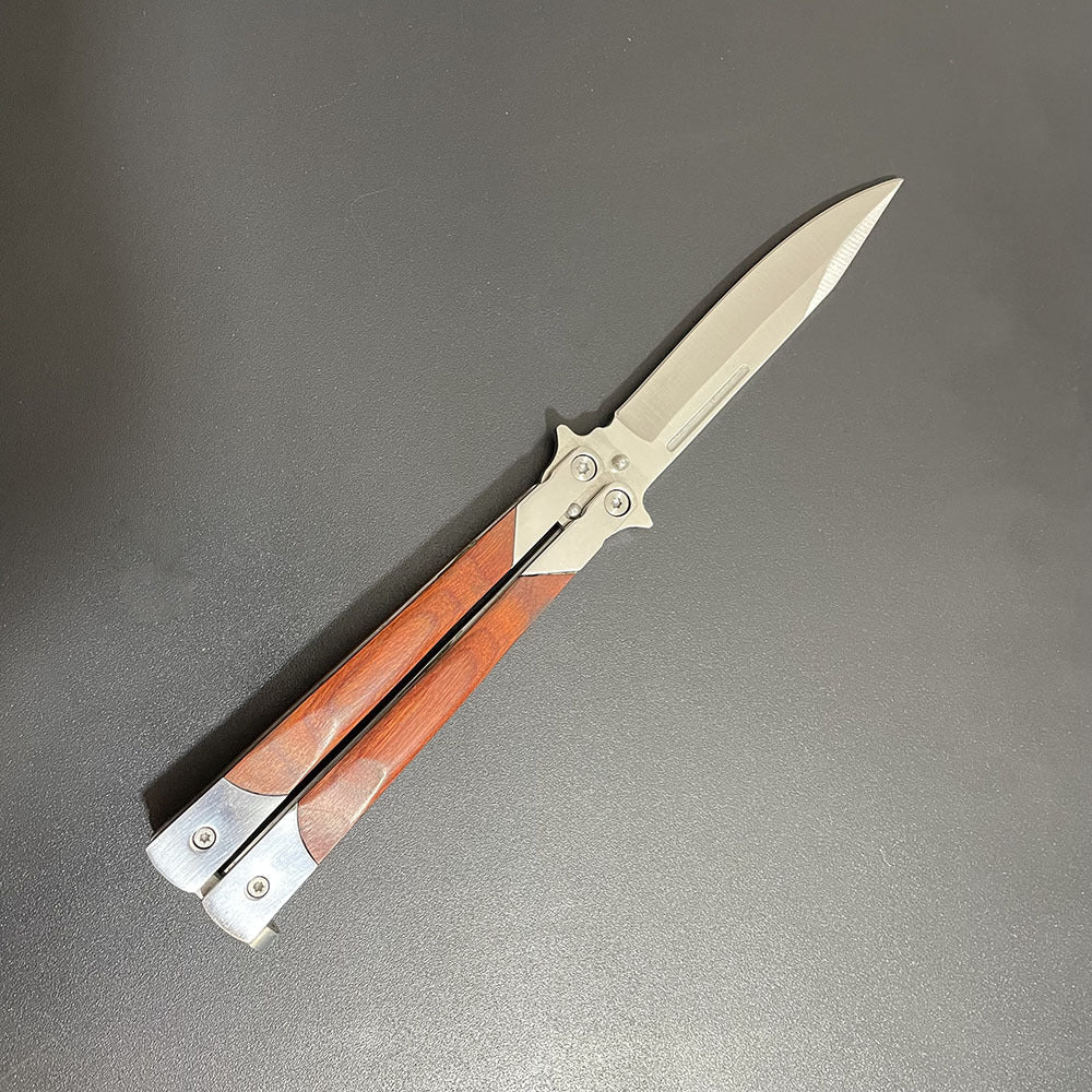 A close-up of an open balisong butterfly knife with a wooden handle and a silver blade, displayed diagonally on a dark background.