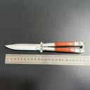 An open balisong butterfly knife with a wooden handle shown next to a metal ruler on a dark surface to display its length dimensions.