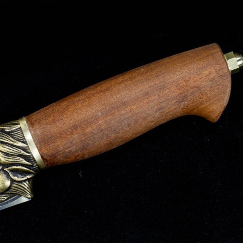 A close-up of a polished wooden knife handle showing the wood grain, brass animal head guard, and a brass pommel at the end of the handle.