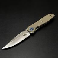 An open Zero Tolerance folding knife with a tan handle, silver blade, and blue pivot screw, displayed on a dark background.