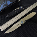 Two Zero Tolerance knives, one closed black and one open tan, displayed next to a metal ruler and a black box on a dark textured surface.