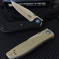 A closed black Zero Tolerance knife and an open tan Zero Tolerance knife, displayed on a dark textured surface with a box and pouch in the background.