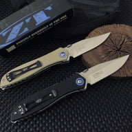 Two open Zero Tolerance knives, one tan and one black, resting on a wooden slice next to a box, showing the blade engraving on the tang.